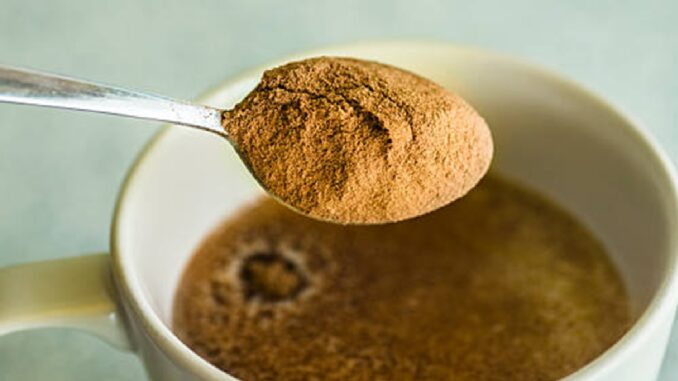 A spoon with powdered cocoa falling on a mug with milk.